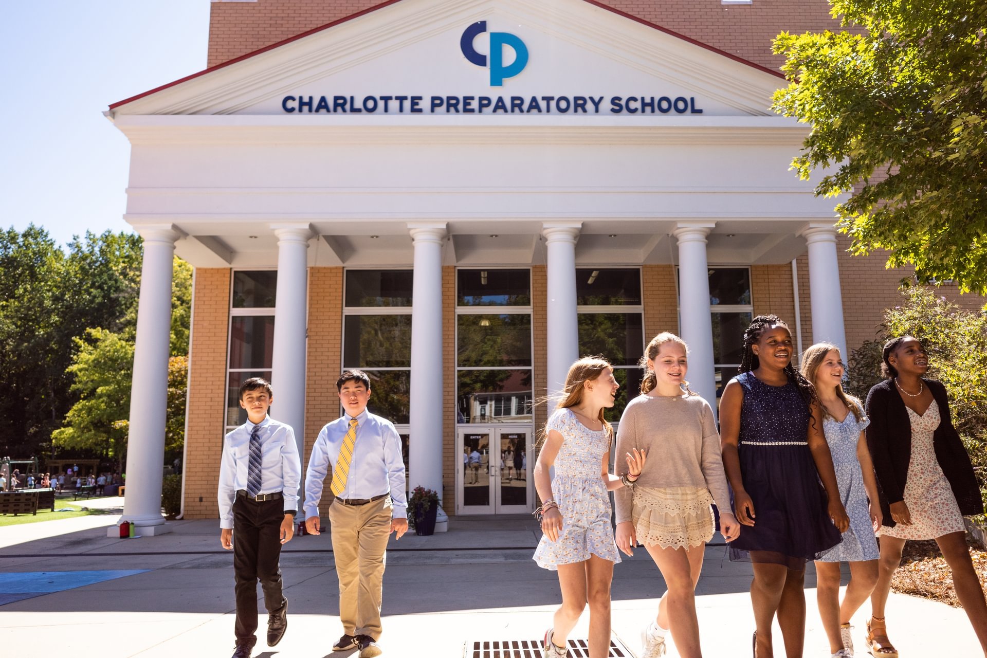 Two groups of students walk outside of a building smiling.